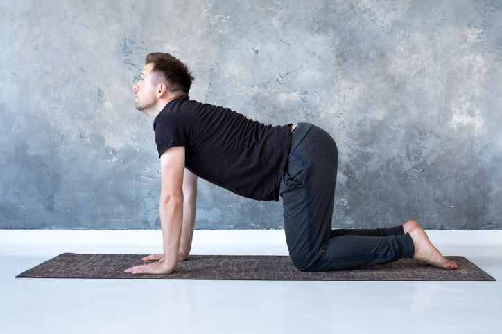 A man performs the cat-cow yoga pose at home.