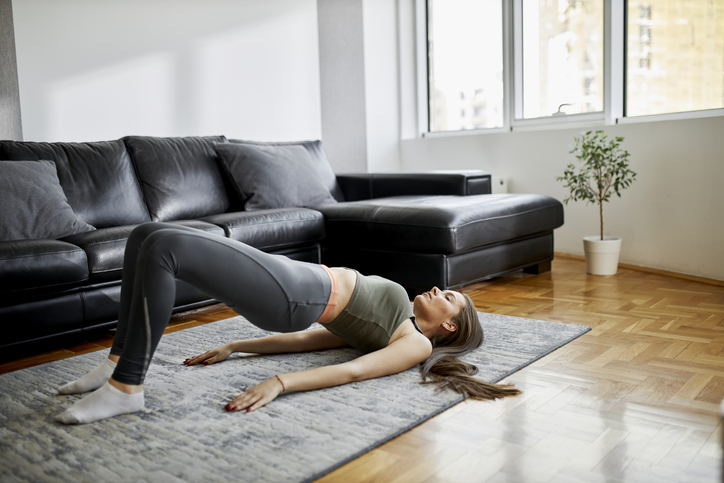 A young woman performs the bridge stretch at home in her living room.