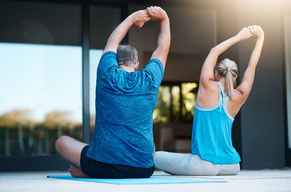 Two people sit with arms reaching upward to stretch the spine.