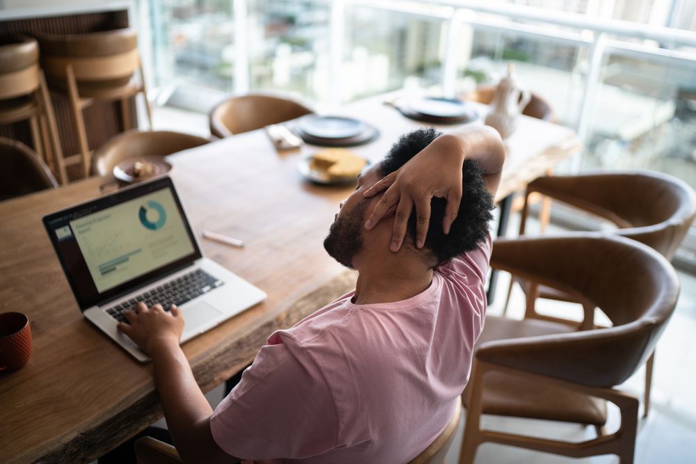 A man sits in front of a computer and stretches his neck to one side.